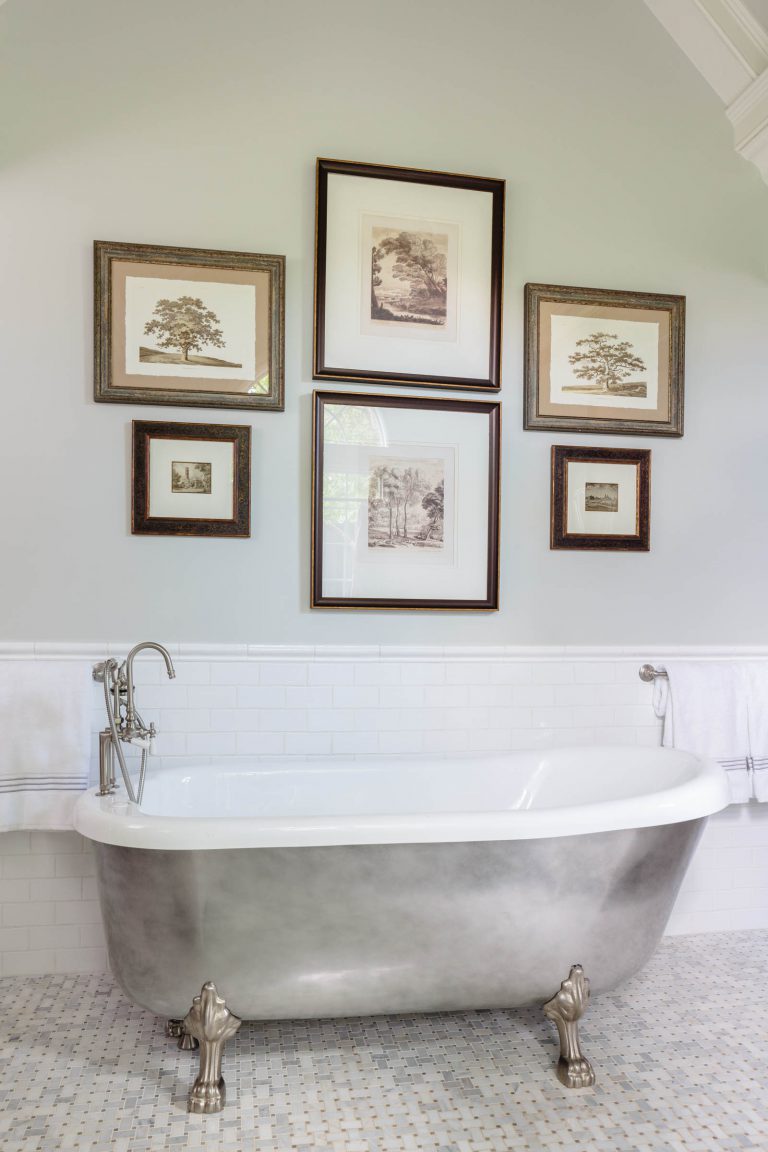 A bathroom with a clawfoot bathtub featuring silver feet and fixtures. The wall behind it is adorned with five framed black and white nature sketches arranged asymmetrically. A white towel hangs from a rack on each side of the tub. The floor is tiled with a mosaic pattern.