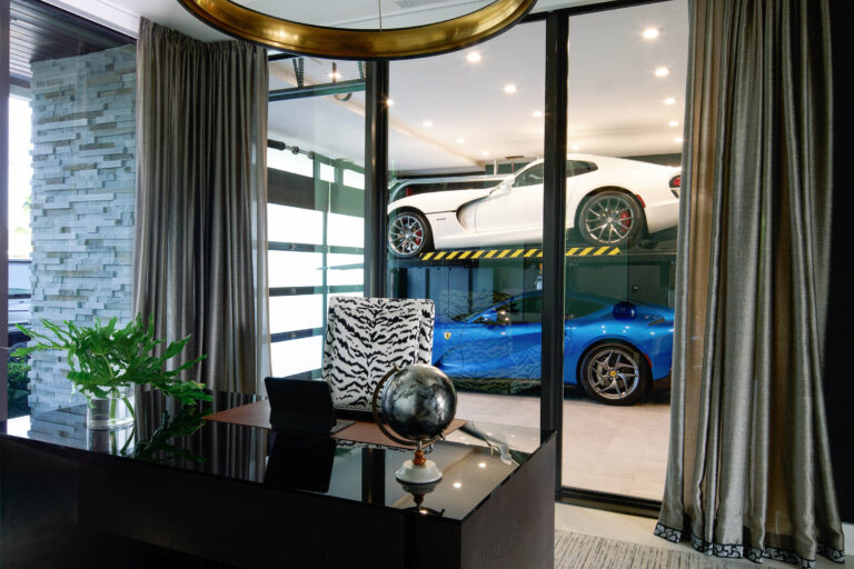 A luxurious room with a black desk and a zebra-print chair. On the desk are a globe and a green plant. Through glass walls, a garage is visible with a white car on top of a lift and a blue Ferrari parked below. Elegant curtains and stone wall panels adorn the room.