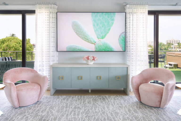 A modern living room with large windows features two pink velvet chairs and a sleek light blue cabinet. Above the cabinet is a large TV displaying an image of green cactus leaves. A vase with pink flowers sits on the cabinet. The room has sheer white curtains and a textured gray rug.